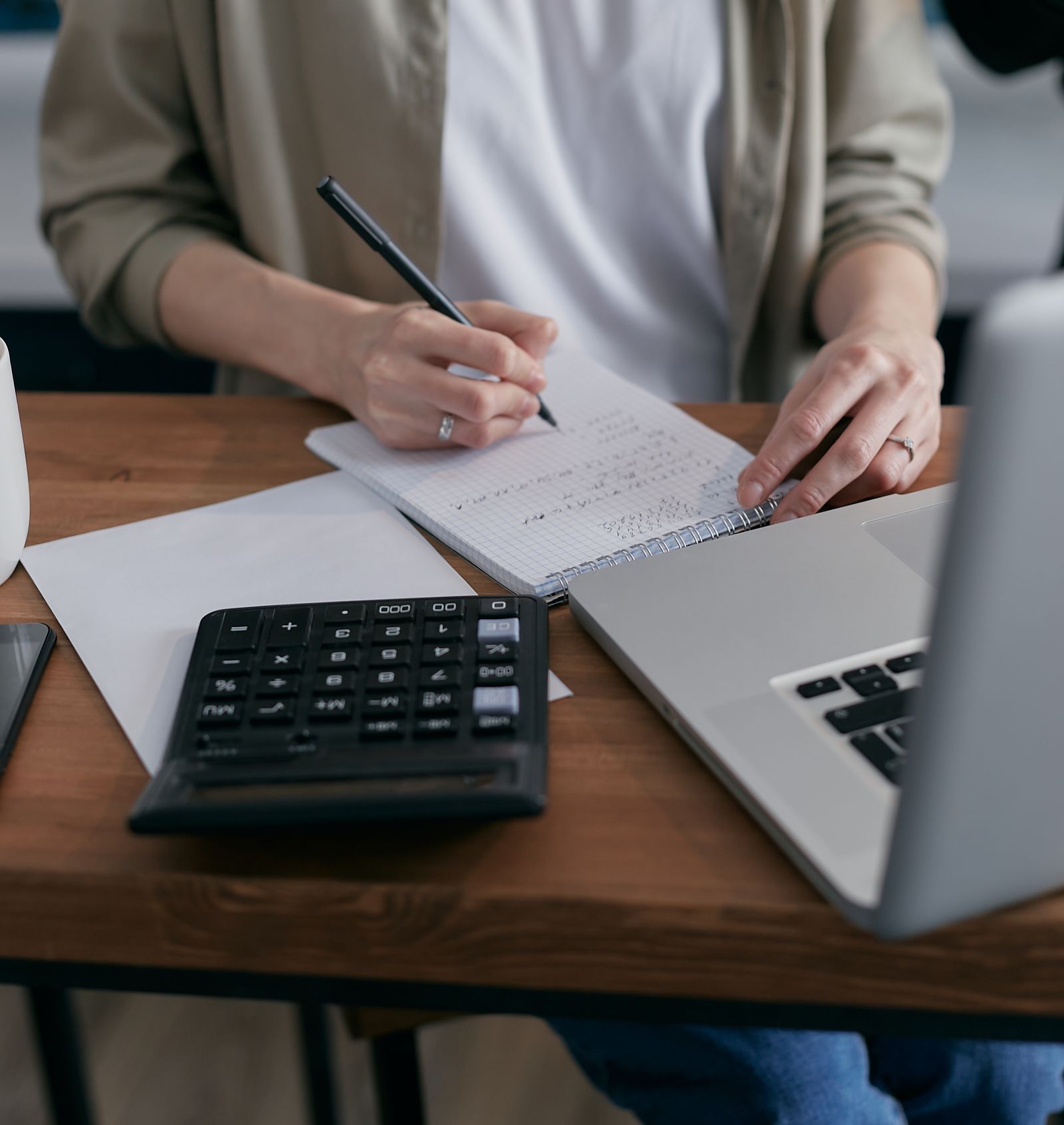 Bookkeeper writing financial calculations with a calculator and laptop