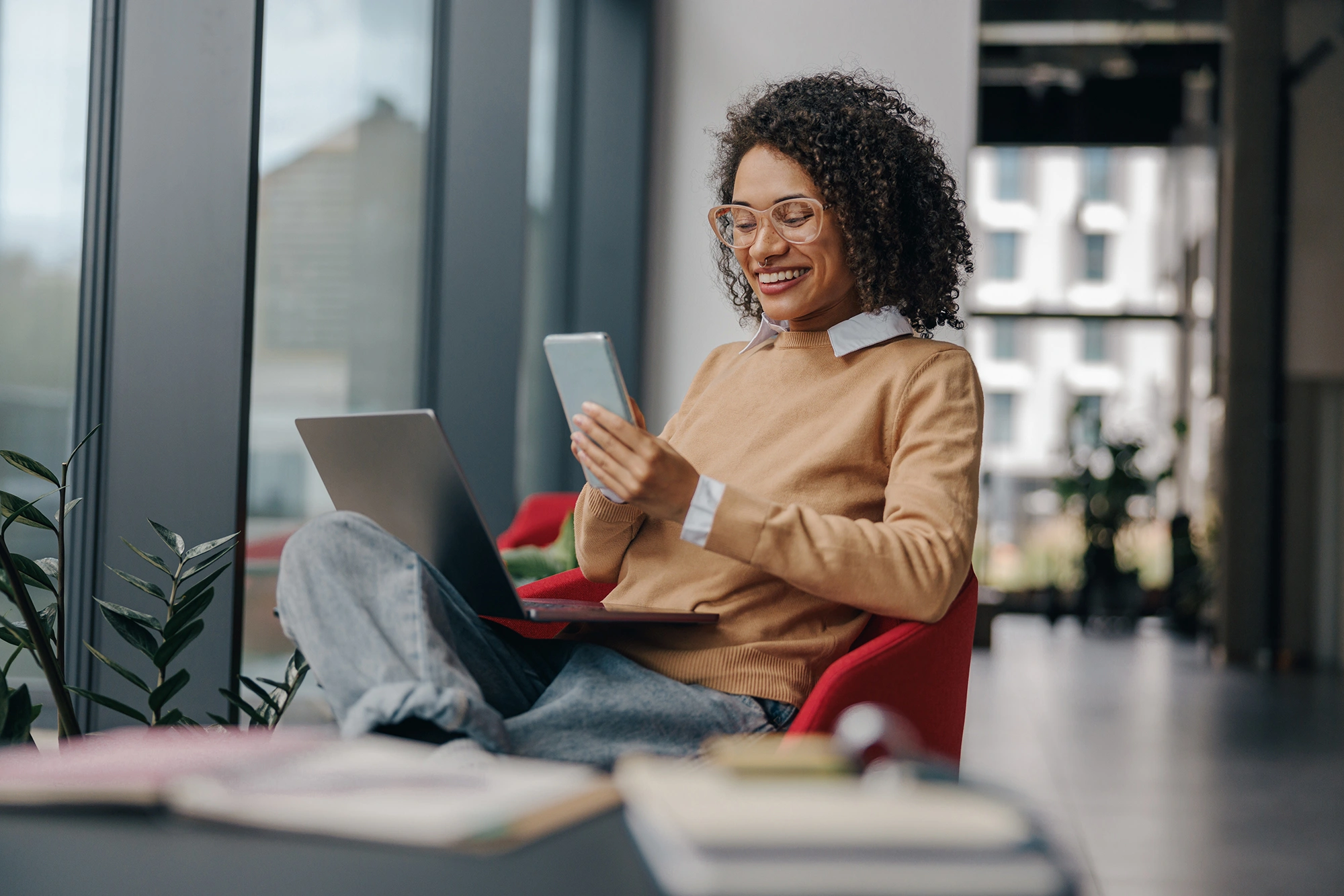 A smiling small-business owner relaxing with a laptop and phone in a bright office